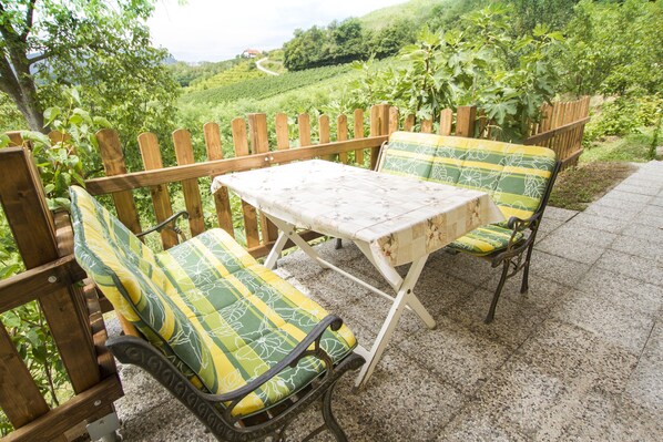 Eine Terrassengruppe im Freien mit Holztisch und zwei Stühlen, umgeben von einem Holzzaun und üppiger Bepflanzung.