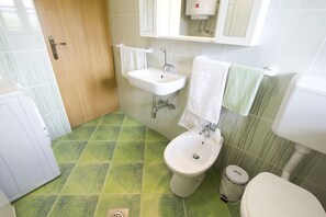 Ein Badezimmer mit grün gefliestem Boden, einem weißen Waschbecken, einem Bidet und einer Toilette.