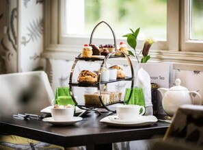 A three-tiered dessert stand with various pastries and a teapot on a table. - Woughton House Hotel, WorldHotels Distinctive (Milton Keynes)