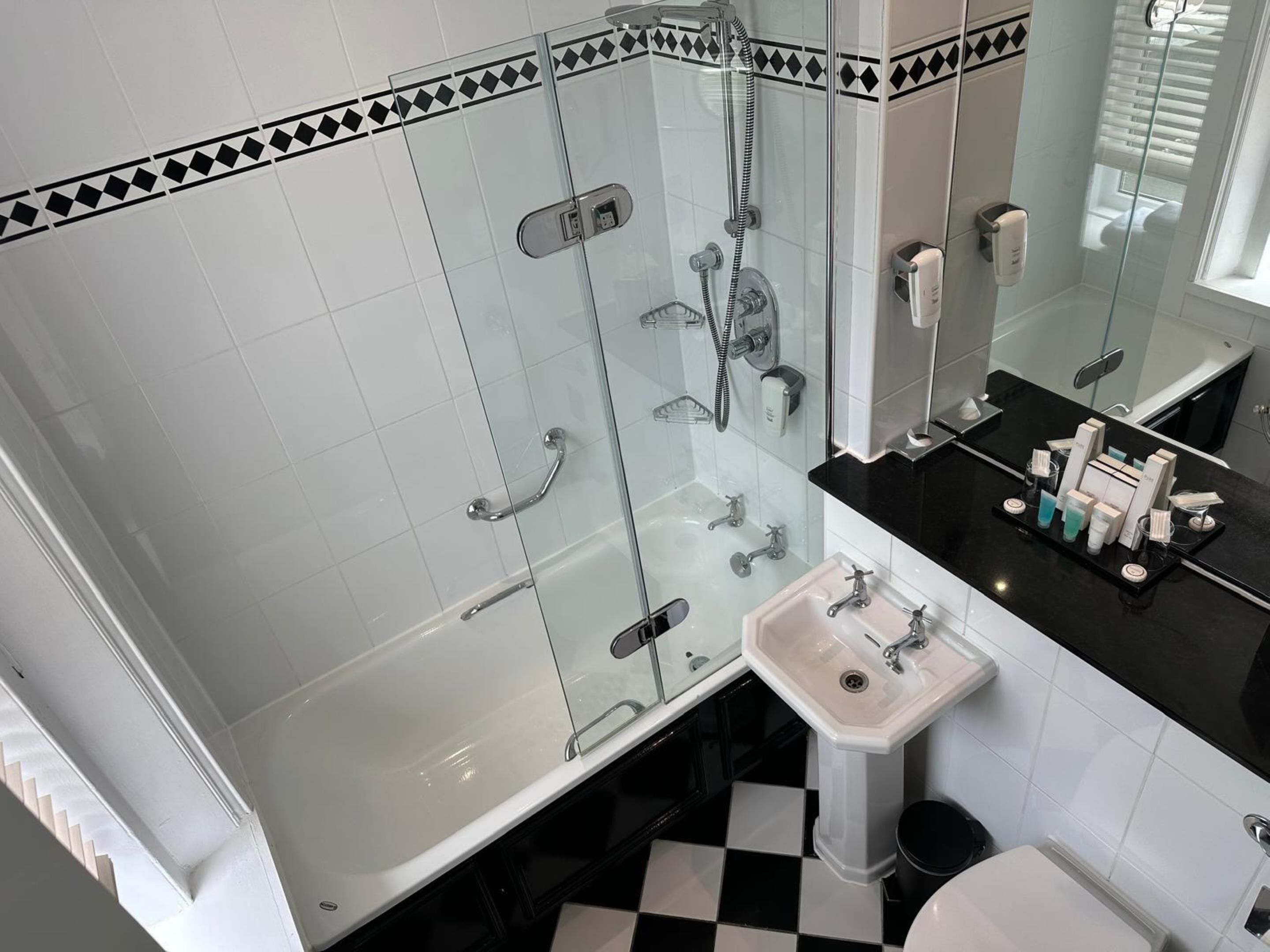 Un baño con ducha envuelta en vidrio, un lavabo blanco y una encimera negra con artículos de aseo.
