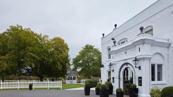 Un edificio blanco con cerca blanca, plantas en macetas y un quiosco de jardín al fondo.