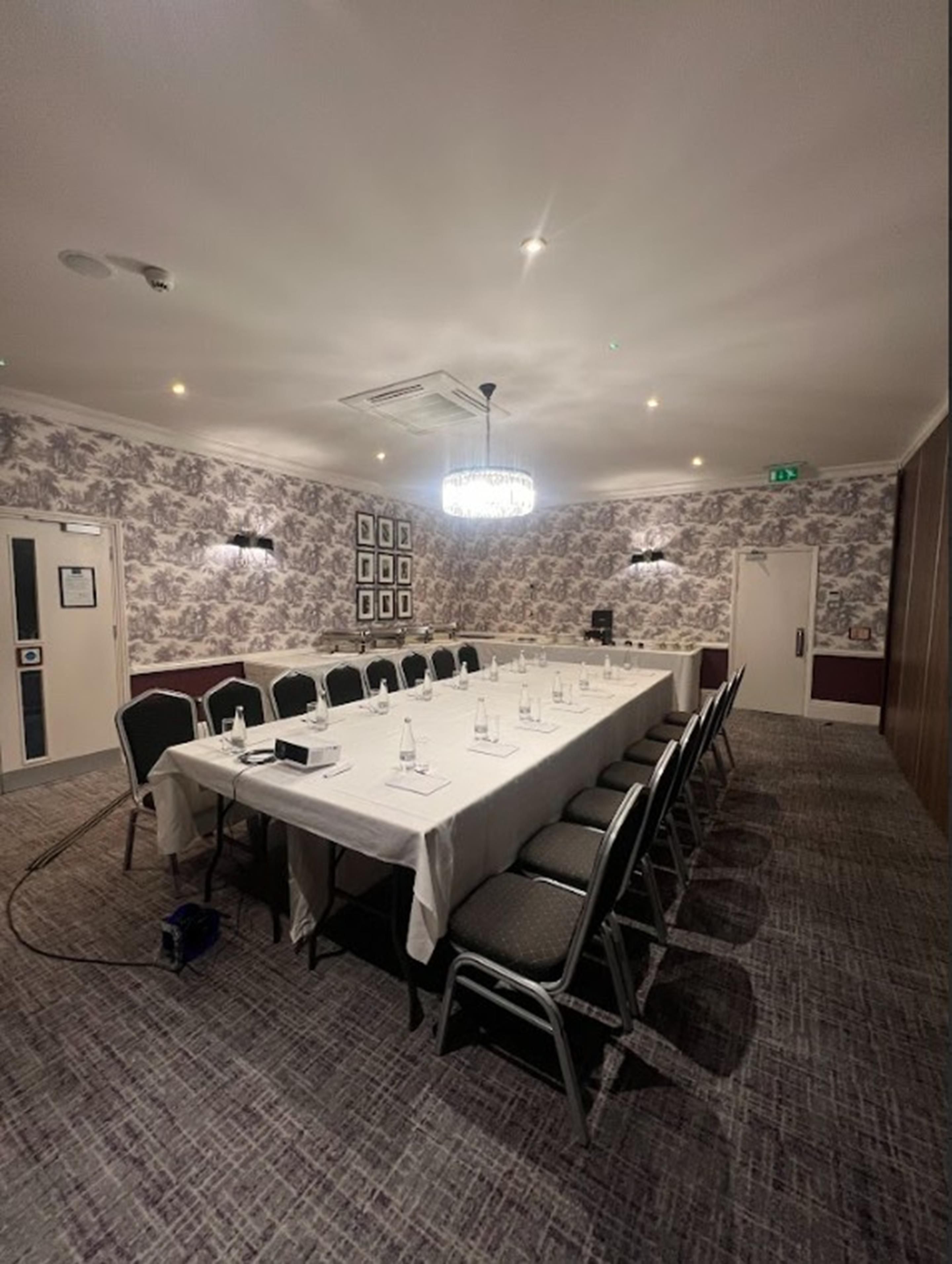 A conference room with a long table, chairs, a chandelier, and patterned wallpaper.