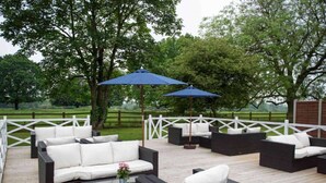 Eine Terrassengruppe mit Korbmöbeln, weißen Kissen und blauen Sonnenschirmen.