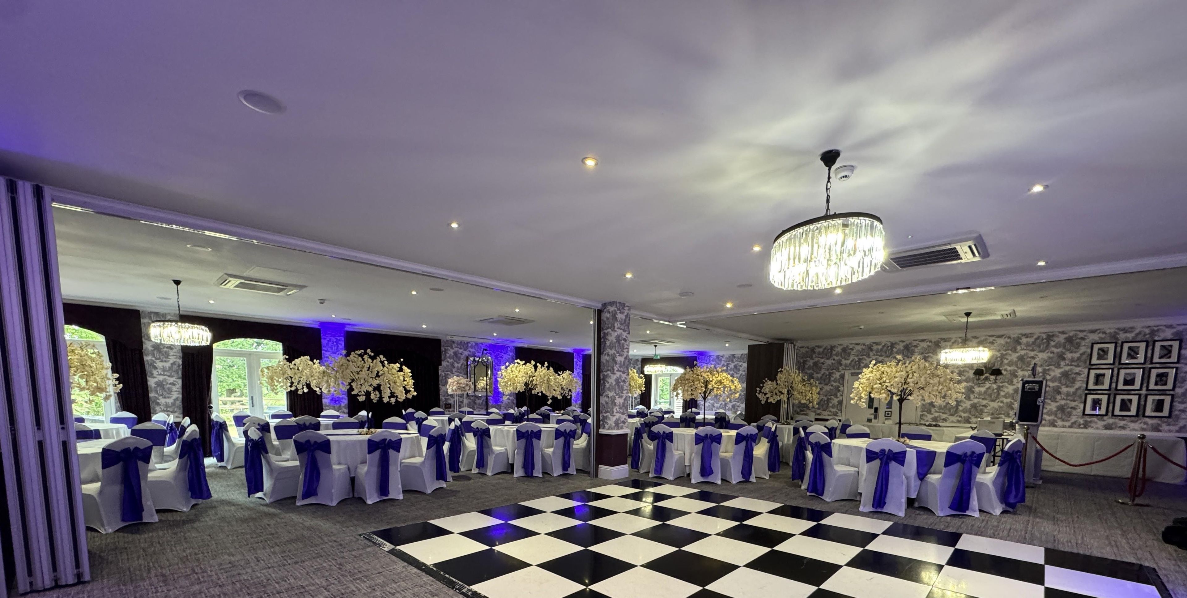A banquet hall with tables arranged in a circular pattern, centered around a checkered dance floor, and adorned with floral arrangements.