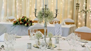 Ein Festtisch, reich gedeckt mit Kristallgläsern, Besteck und einer Blumenarrangements als Mittelstück.