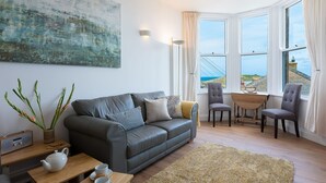 Ein modernes Wohnzimmer mit einer grauen Ledersofa, einem Holztisch und Meerblick durch große Fenster.