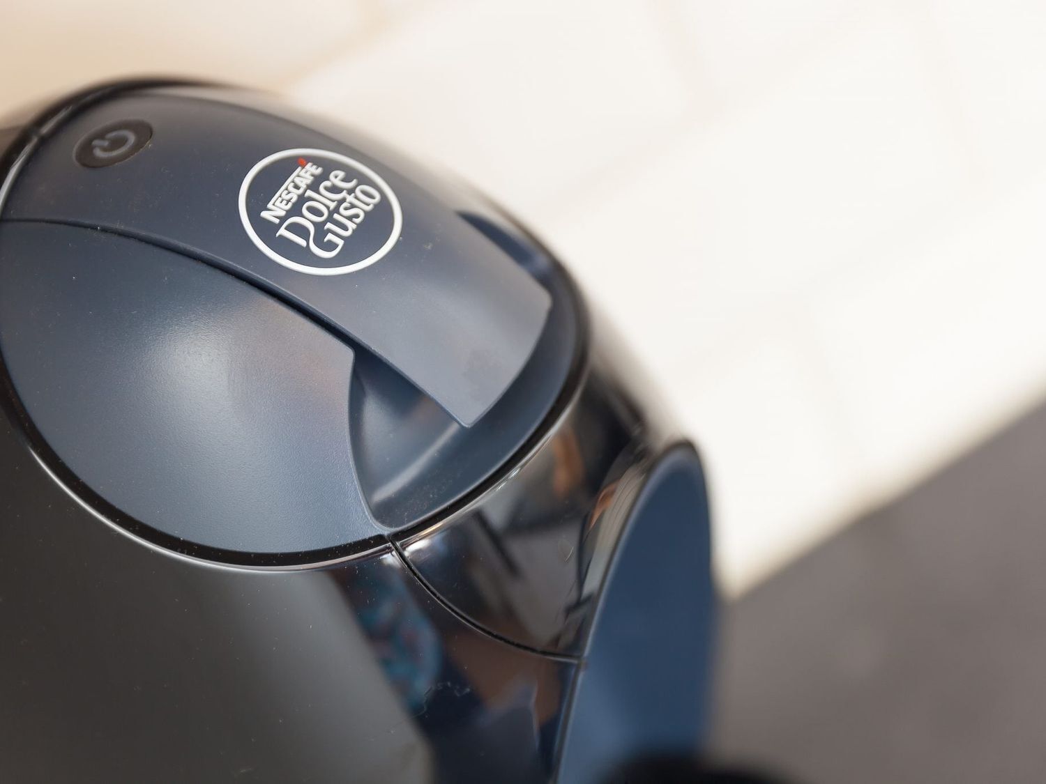 A close-up of a black coffee machine with a circular logo that reads "Nescafe Dolce Gusto".