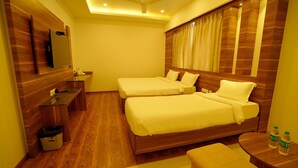 A hotel room with two beds, a desk, a chair, a small table, a trash bin, and a ceiling fan. - Springs Hotel (Tirupati)