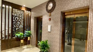 A modern lobby with a wooden panel wall, a decorative wall clock, and potted plants. - Springs Hotel (Tirupati)