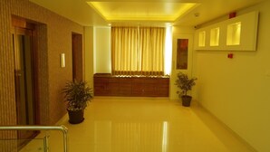 A modern hallway with a wooden panel wall, a central seating area with curtains, and potted plants. - Springs Hotel (Tirupati)