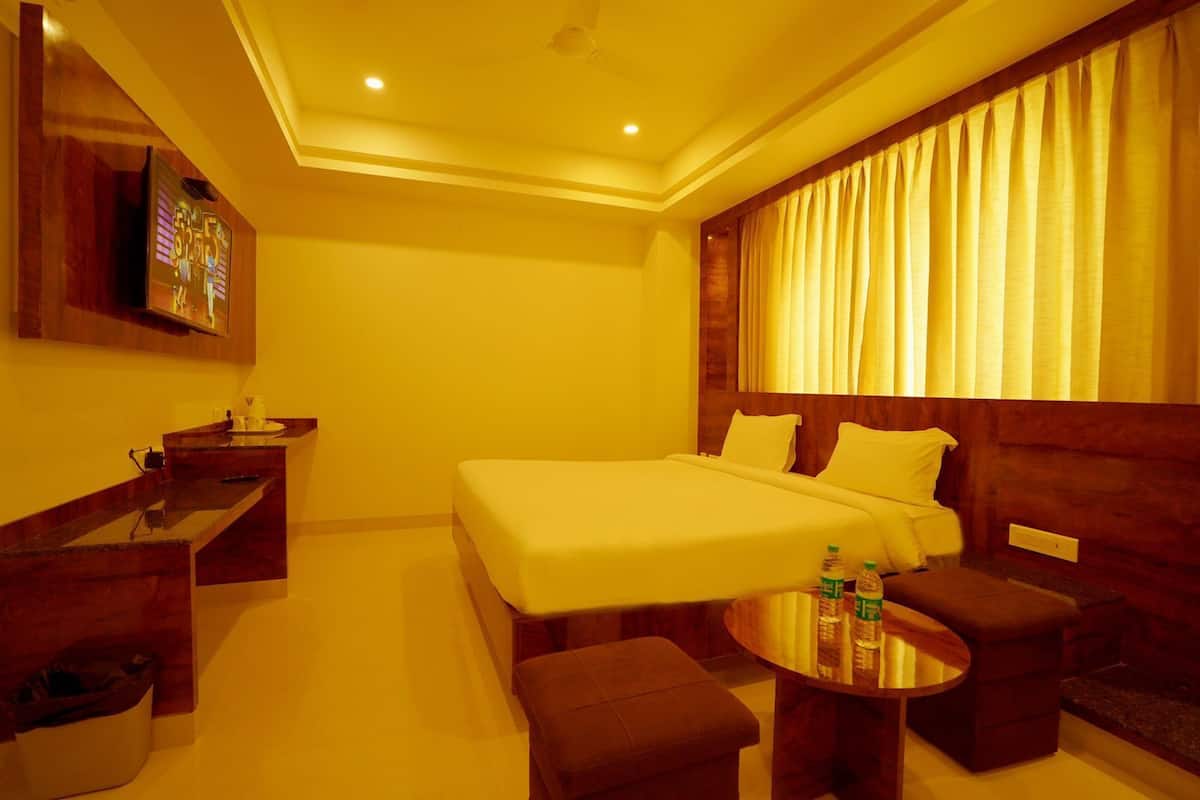 Quarto de hotel com cama, escrivaninha, cadeira, mesinha e televisão.