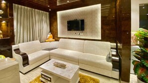A modern living room with a sectional sofa, a flat-screen TV mounted on a textured wall, and a decorative coffee table. - Springs Hotel (Tirupati)