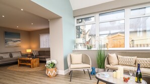 Een moderne woonkamer met een bank, fauteuils, een salontafel en uitzicht op buiten.