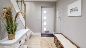 Een hal met een trap, een witte console tafel, een gevlochten mand, een ingelijst kunstwerk en een deur met een zwarte mat.