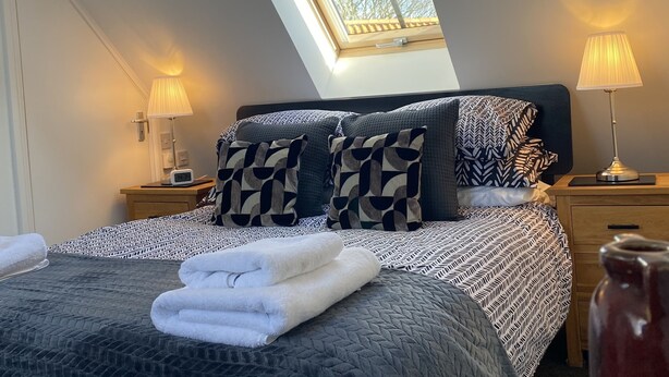 A bedroom with a skylight, a bed with patterned bedding, two bedside lamps, and a bedside table with a lamp and a phone. - Flemings Yard - Fantastic Town House in Anstruther (Anstruther)
