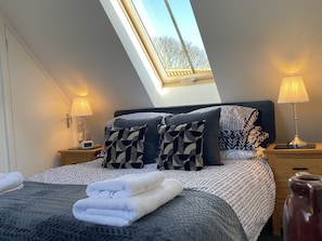 A bedroom with a skylight, a bed with patterned bedding, two bedside lamps, and a bedside table with a lamp and a phone. - Flemings Yard - Fantastic Town House in Anstruther (Anstruther)