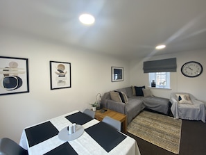 A modern living room with a sofa, a dining table with a black and white checkered tablecloth, and a clock on the wall. - Flemings Yard - Fantastic Town House in Anstruther (Anstruther)