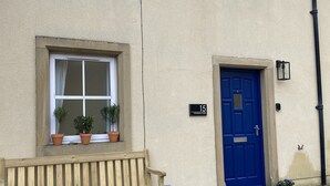 A building with a blue door, a window with potted plants, and a wooden bench outside. - Flemings Yard - Fantastic Town House in Anstruther (Anstruther)