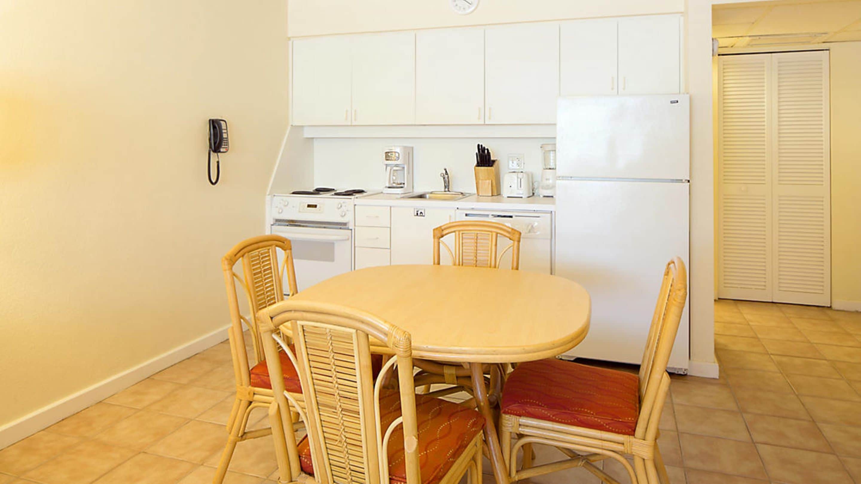 A compact kitchen with white cabinets, a stove, a refrigerator, and a dining table with four chairs.