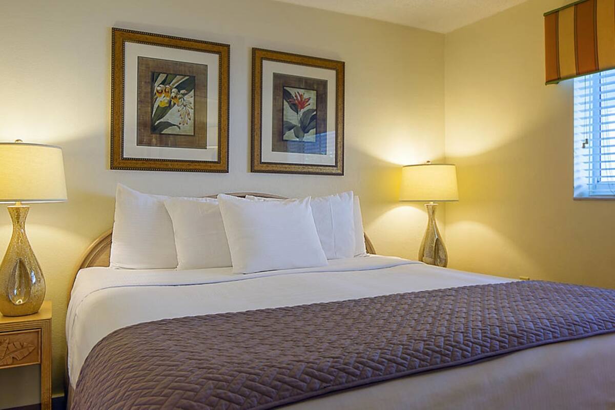 A hotel room with a bed, two bedside lamps, a nightstand, and two framed pictures on the wall.