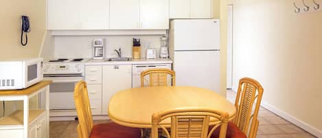 A compact kitchen with white cabinets, a microwave, a stove, a refrigerator, and a dining table with four chairs.