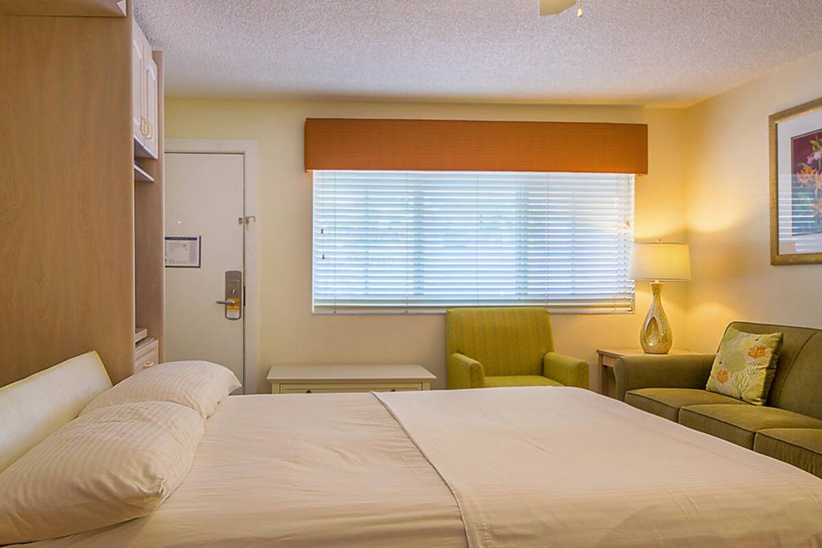 A hotel room with a bed, a chair, a desk, and a window with blinds.