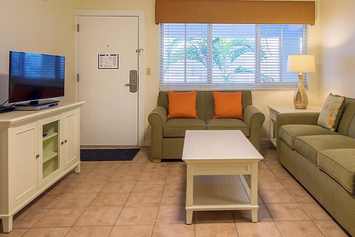 A living room with two sofas, a coffee table, a TV on a cabinet, and a window with blinds.