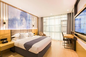 Quarto de hotel moderno com uma cama grande, mesa de cabeceira, escrivaninha com cadeira, televisão e uma grande obra de arte abstrata na parede.