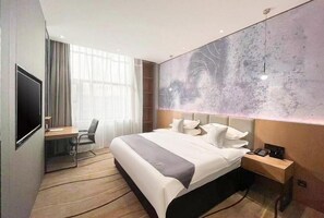 Moderni hotellihuone, jossa on suuri sänky, työpöytä ja televisio.
