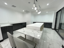 A modern kitchen with a marble countertop, dark cabinetry, and a glass door leading to a balcony.