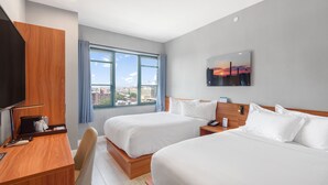 A hotel room with two beds, a desk, a chair, a TV, and a window with a city view. - Liberty View Brooklyn hotel (Brooklyn)