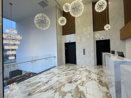 A modern lobby with marble flooring, a glass railing, and multiple chandeliers.