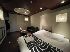A modern hotel room with a large bed, a black leather sofa, a small table, and a headboard with built-in lighting. - HOTEL Fuuga Luxury Resort - Adults Only (Maizuru)