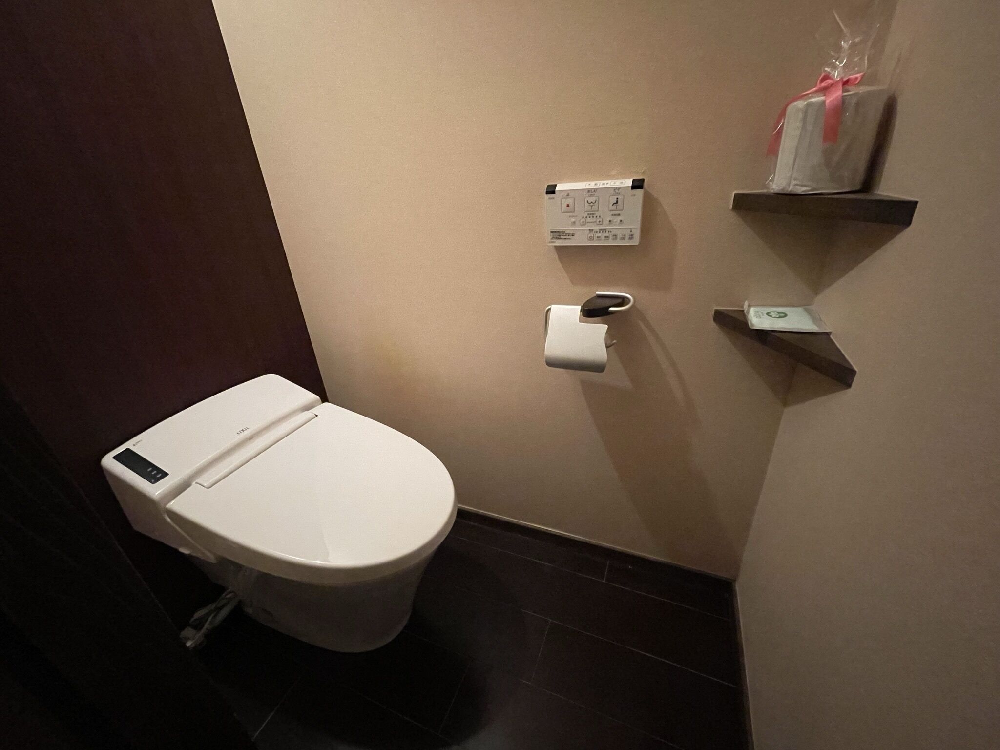 Ein modernes Badezimmer mit Toilette, einer an der Wand montierten Spültaste und einer kleinen Ablage mit einer Geschenkverpackung.