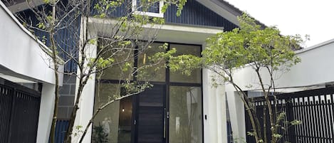 Una casa moderna con un gran ventanal, un pequeño porche y un camino de piedra que lleva a la entrada.