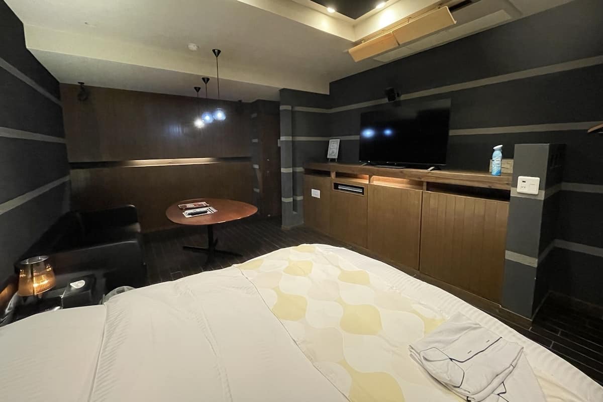 A hotel room with a bed, a small round table, a sofa, a TV, and a minibar.