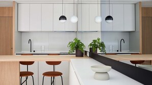 A modern kitchen with white cabinets, black pendant lights, a central island with stools, and two potted plants. - 60 Balconies Iconic (Madrid)