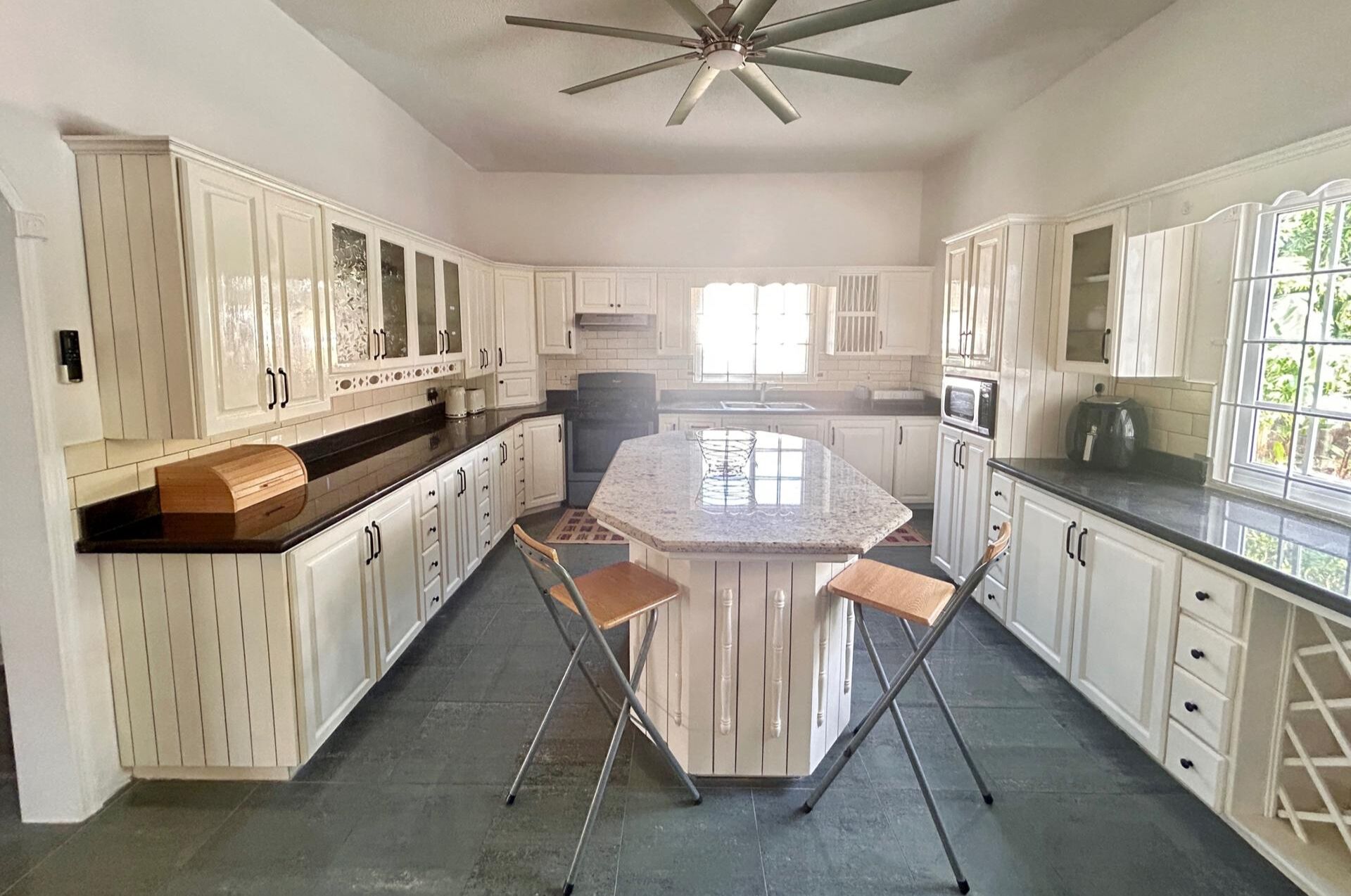 A spacious kitchen with white cabinetry, a central island, and a ceiling fan.