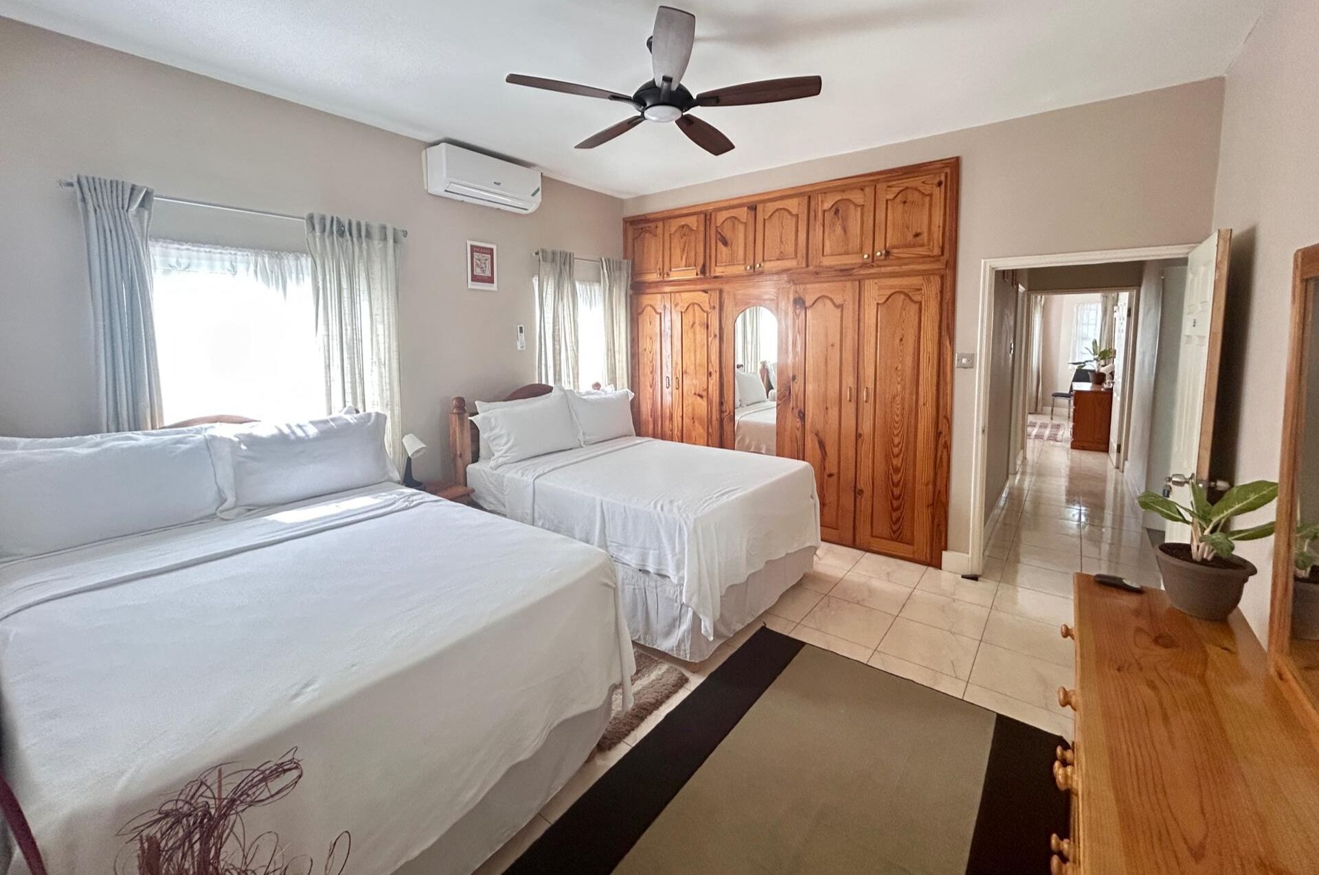 Une chambre d’hôtel avec deux lits, un ventilateur de plafond, une armoire en bois et une plante en pot.