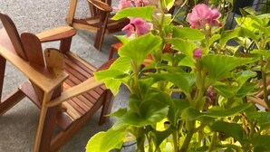 A covered outdoor seating area with wooden chairs, a potted plant with pink flowers, and a metal sculpture. - Hotel La Vid (La Fortuna)