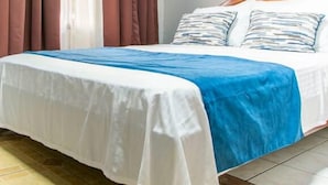 A bed with a white and blue bedspread, brown curtains, and a painting on the wall. - Hotel La Vid (La Fortuna)