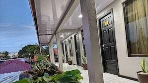 A covered outdoor area with potted plants, a tiled floor, and a black door with a sign above it. - Hotel La Vid (La Fortuna)