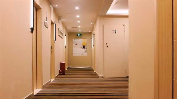 Corredor de hotel com piso carpetado, portas em ambos os lados e uma placa no final.