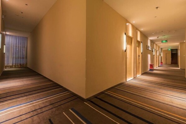 A hotel corridor with striped carpet, beige walls, and a long hallway with doors and lights. - City Comfort Inn Haikou East High Speed Railway Station (Haikou)