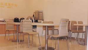 Een moderne eetruimte met meerdere tafels en stoelen, een balie met een kassa en een muur met tekst.