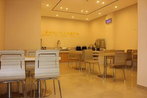A modern, well-lit dining area with a long counter, multiple chairs, and a small kitchen area in the background.