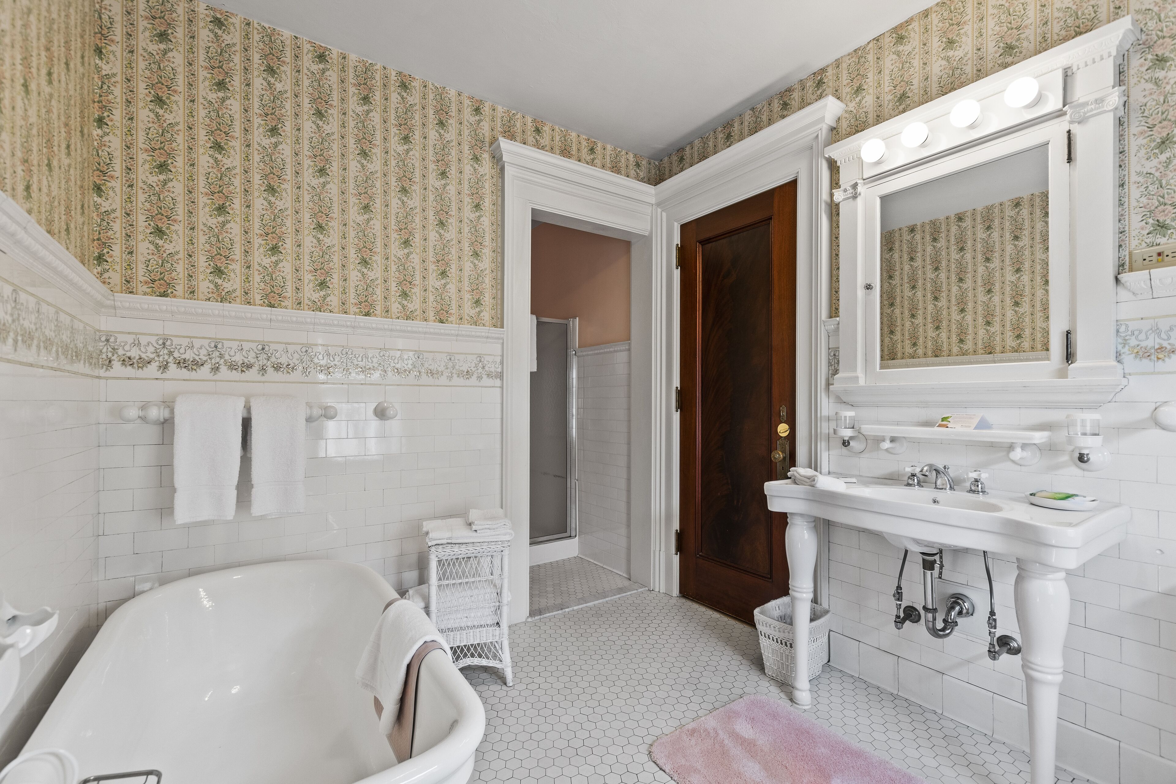 A bathroom with a freestanding bathtub, a vanity with a mirror and lights, and a shower area.