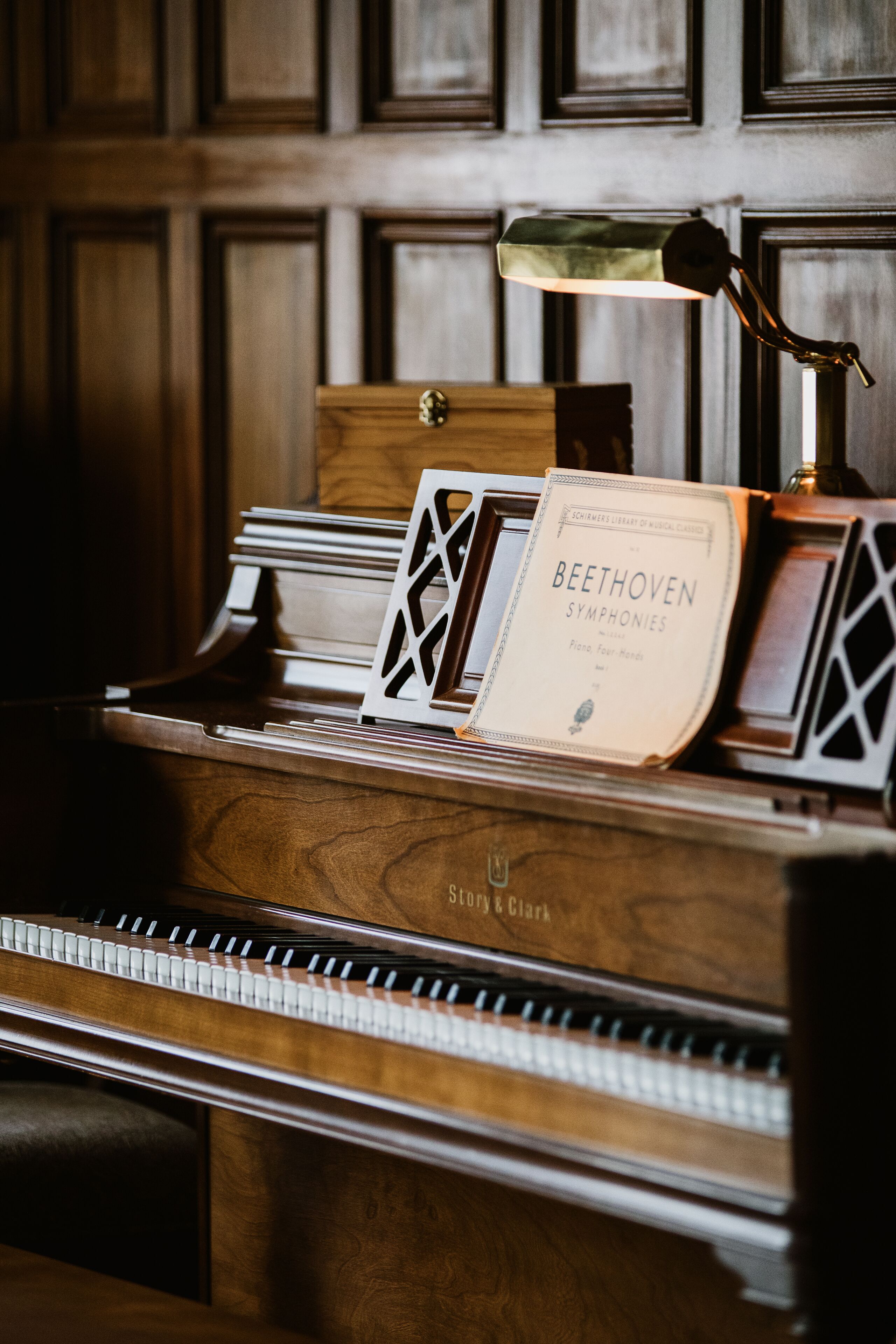 Un piano de cola con partituras tituladas "Sinfonías de Beethoven" y una lámpara encima.