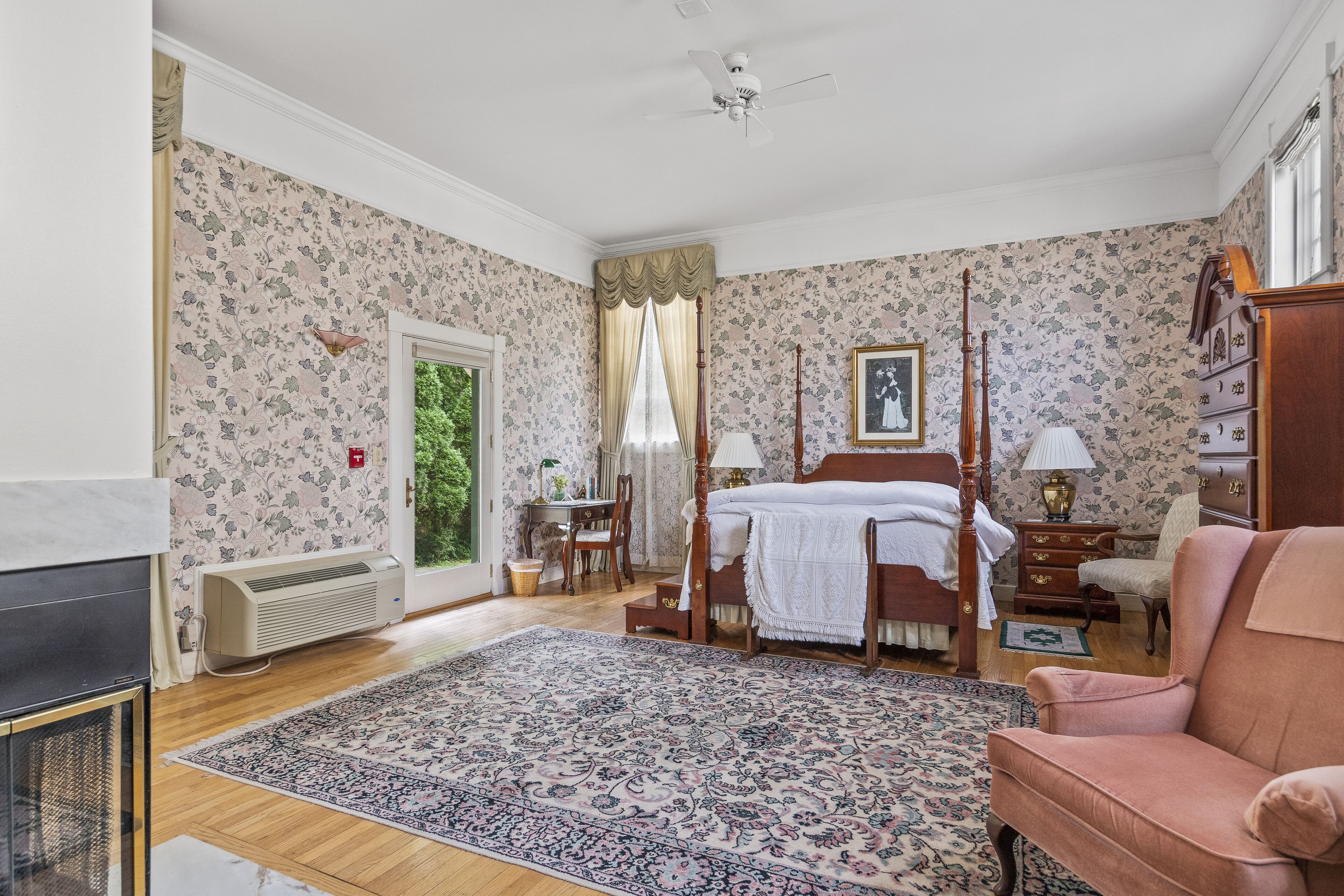 Un dormitorio con una cama con dosel, una silla de madera, un escritorio, un radiador y una chimenea.