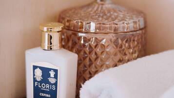 Una botella blanca de crema corporal Floris sobre una estantería, junto a un recipiente de vidrio texturizado.
